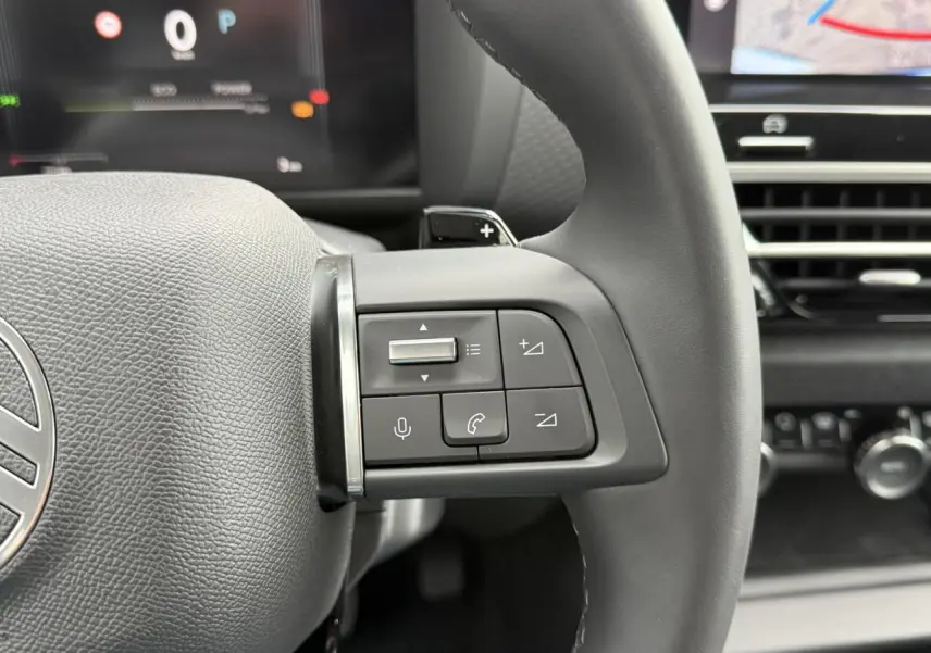 Gros plan sur les commandes au volant côté droit du Citroën C4 hybride 2025 avec tableau de bord numérique en arrière-plan.