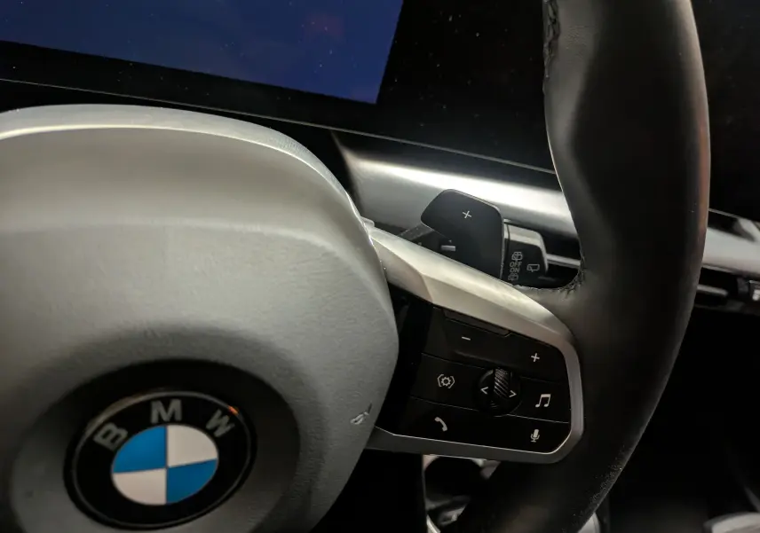 Gros plan sur le volant cuir M de la BMW X1 blanc, avec commandes multifonctions et palettes au volant visibles.