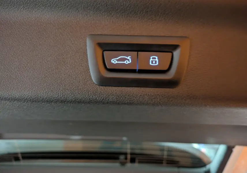 Gros plan sur les boutons d'ouverture et de verrouillage du coffre du BMW X1 blanc, vue intérieure arrière.