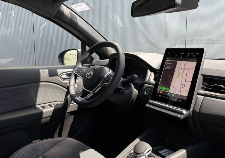 Intérieur du Renault Captur hybride 2025 côté conducteur, volant cuir multifonctions et écran tactile vertical avec navigation.