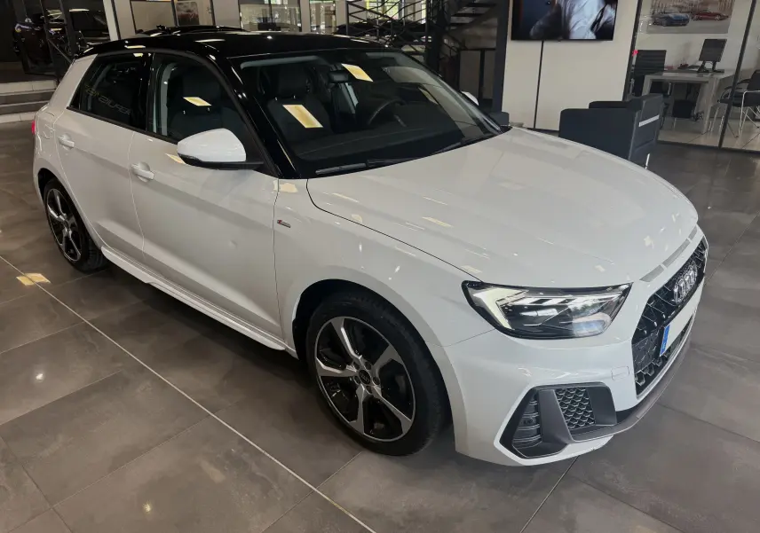 Audi A1 30 TFSI S-Line blanche avec toit noir vue 3/4 avant droit en intérieur showroom, jantes noires distinctives.