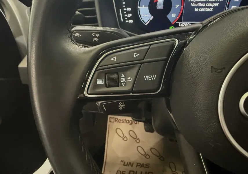 Gros plan sur le volant multifonction de l'Audi A1 30 TFSI blanche, avec affichage numérique du tableau de bord en arrière-plan.