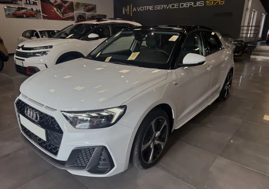 Audi A1 30 TFSI S-Line blanche avec toit noir, vue 3/4 avant droit en intérieur de showroom.