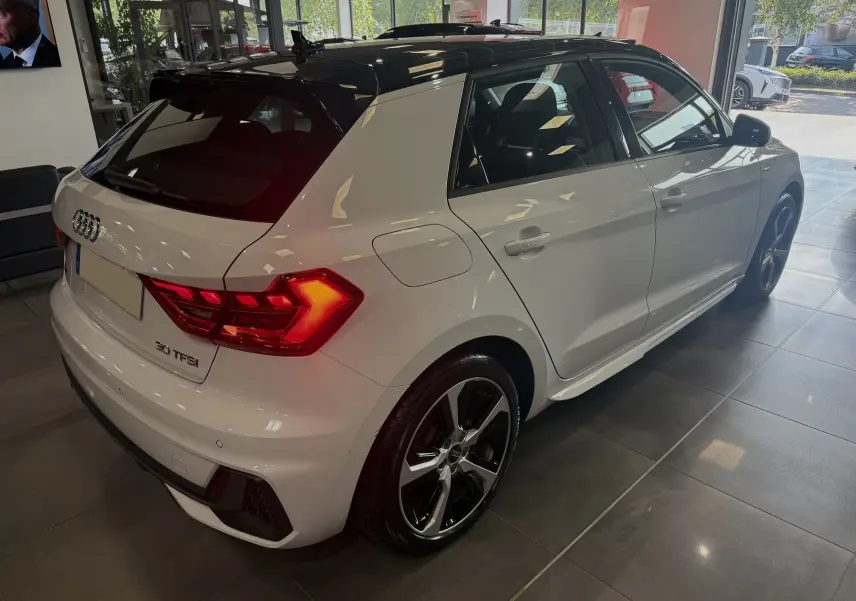 Audi A1 30 TFSI S-Line blanche avec toit noir, vue 3/4 arrière droit en showroom lumineux.