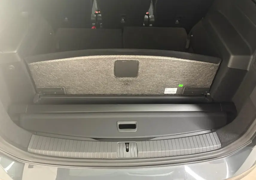 Coffre ouvert du Volkswagen Touran gris dauphin 2025, montrant la protection de chargement et la banquette arrière rabattue.