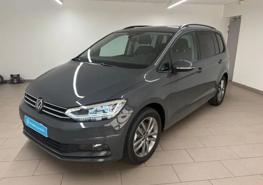 Volkswagen Touran gris dauphin en 3/4 avant droit dans un intérieur, avec jantes alliage et phares LED allumés.