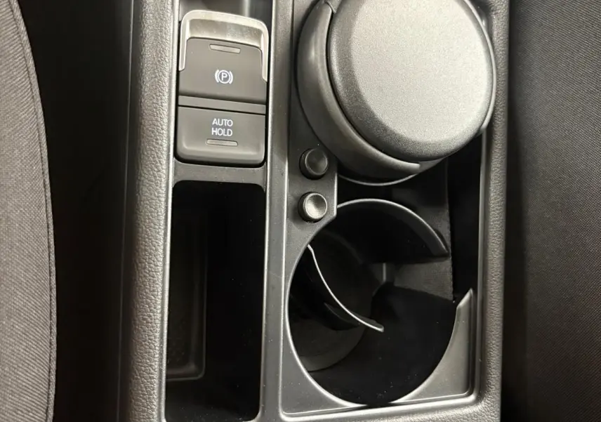 Gros plan sur la console centrale noire du Volkswagen Touran 2025, avec bouton frein à main électrique et porte-gobelet.