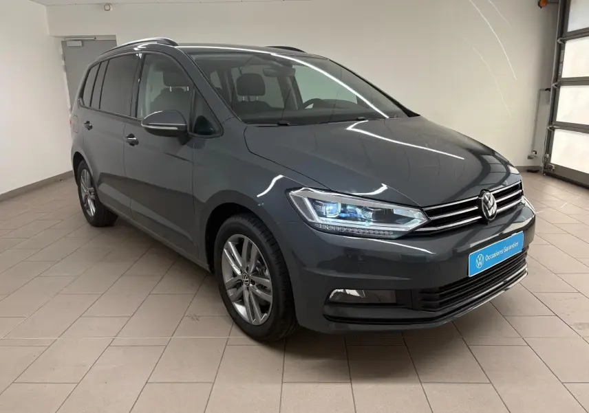 Vue 3/4 avant droit d'un Volkswagen Touran gris dauphin 2025 avec feux LED et jantes alliage 17 pouces.