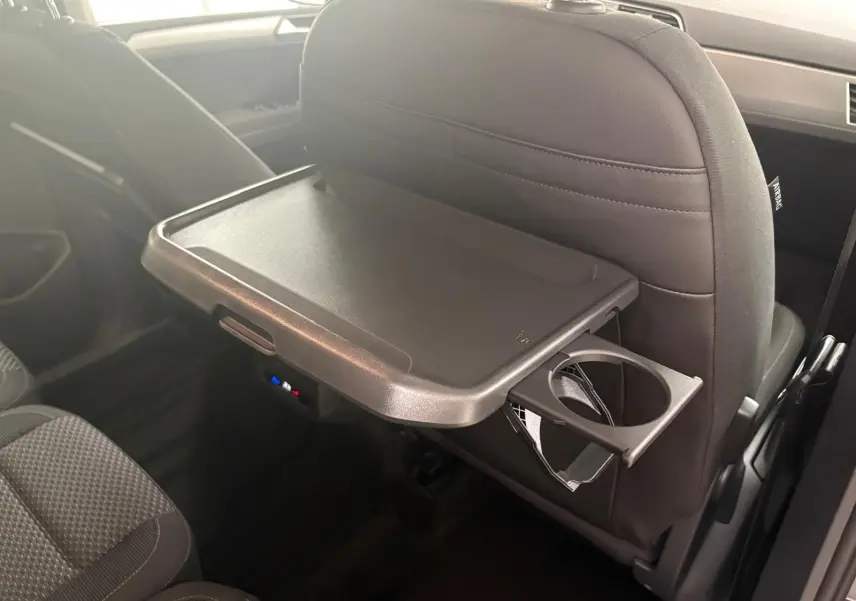 Tablette rabattable avec porte-gobelet fixée au dossier du siège avant dans l'habitacle du Volkswagen Touran gris dauphin.