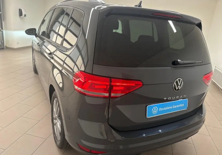 Vue 3/4 arrière gauche d'un Volkswagen Touran gris dauphin avec feux LED et hayon fermé en intérieur showroom.