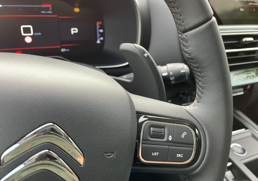 Gros plan sur le volant noir du Citroën C5 Aircross Hybrid 2025 avec commandes intégrées et tableau de bord numérique.