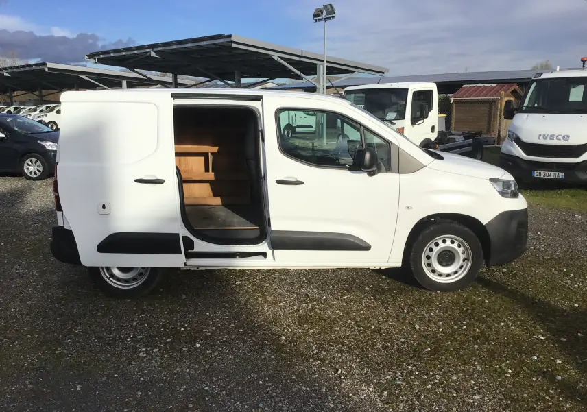 Vue de profil droit d’un utilitaire Citroën Berlingo blanc 2019 avec porte latérale coulissante ouverte montrant l’aménagement intérieur en bois.