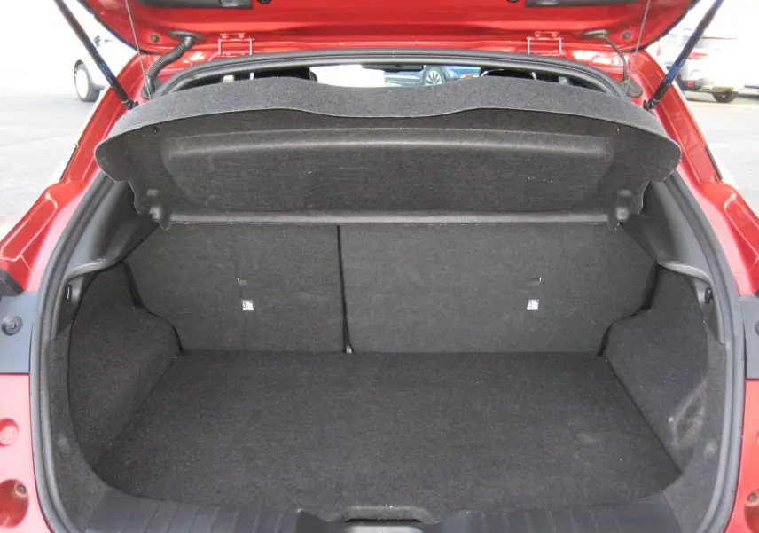 Coffre ouvert vu de l'arrière d'un Nissan Juke 1.6 Hybrid 143 Tekna rouge, montrant un espace de chargement vide et propre.
