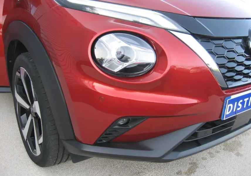 Gros plan sur l’avant droit du Nissan Juke 1.6 Hybrid rouge 2024, mettant en valeur le phare rond et la calandre noire.