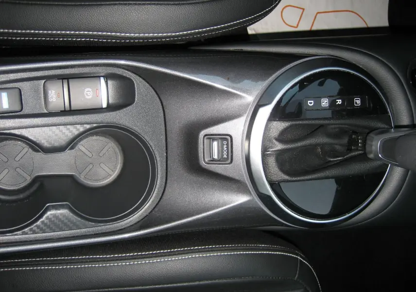 Vue plongeante sur la console centrale noire du Nissan Juke 1.6 Hybrid 143 Tekna avec levier de vitesse automatique et porte-gobelets.