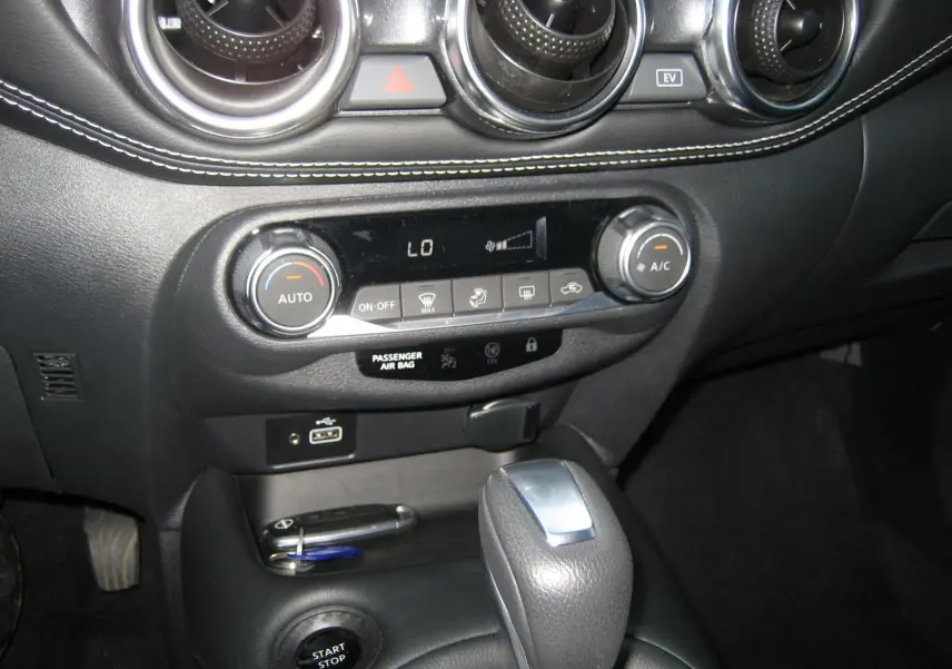 Gros plan sur la console centrale du Nissan Juke rouge 2024, montrant la commande de climatisation et le levier de vitesse automatique.
