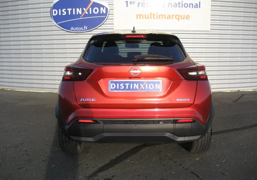 Vue arrière d'un Nissan Juke 1.6 Hybrid 143 Tekna rouge, avec feux arrière LED et logo hybride visible.