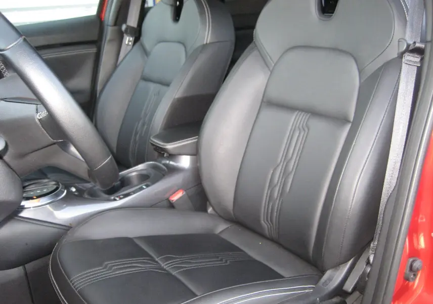 Vue intérieure côté conducteur du Nissan Juke rouge 2024, mettant en valeur les sièges en cuir noir avec surpiqûres décoratives.