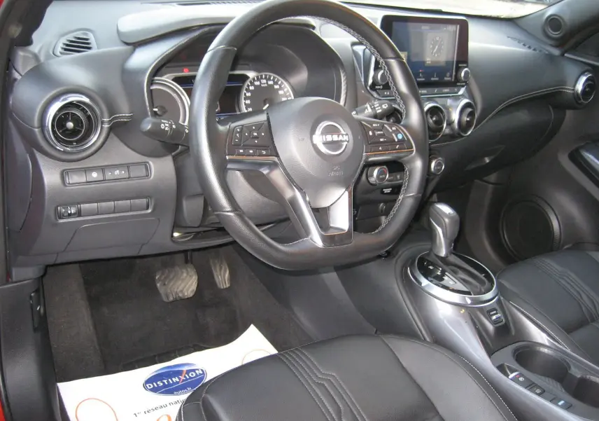 Vue intérieure côté conducteur du Nissan Juke 1.6 Hybrid 2024, avec volant cuir, tableau de bord numérique et console centrale moderne.