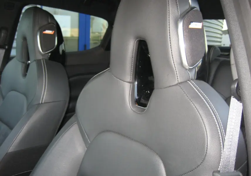 Gros plan sur les sièges avant en cuir noir du Nissan Juke 1.6 Hybrid 143 Tekna, soulignant les surpiqûres blanches et appuie-têtes intégrés.