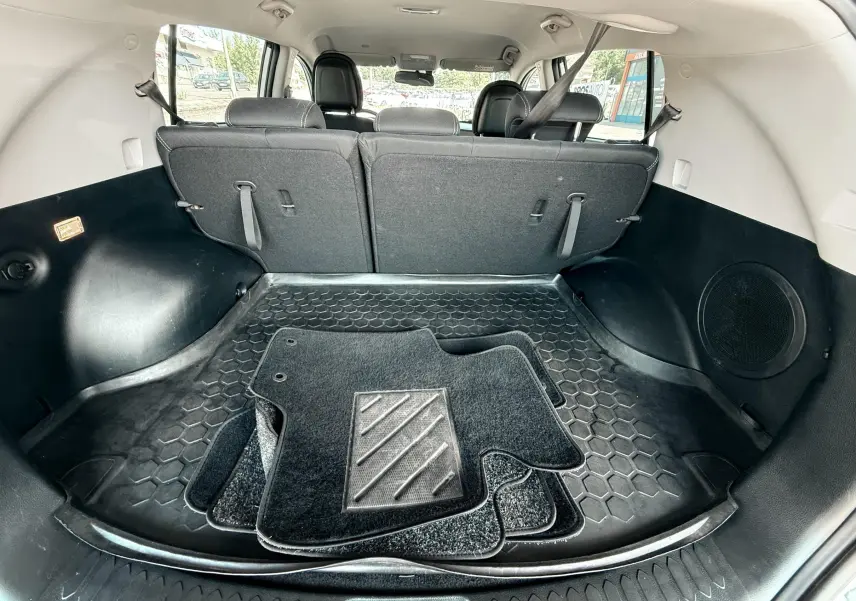 Coffre spacieux du Kia Sportage blanc 2015, vue arrière avec tapis de sol noirs posés à plat.