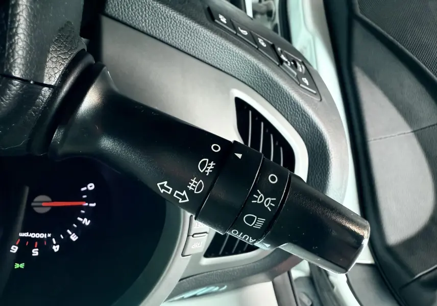 Gros plan sur la manette de commande des phares et clignotants dans l'habitacle d'un Kia Sportage blanc de 2015.