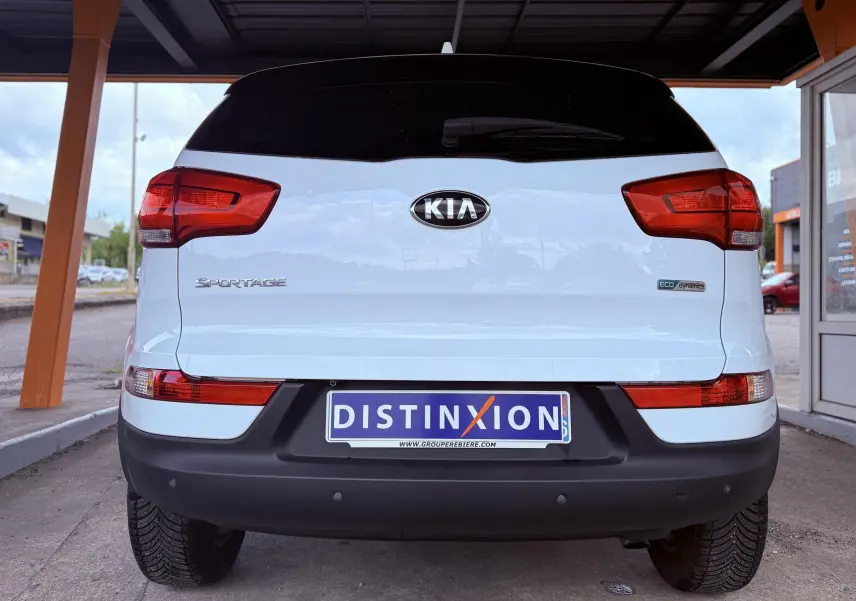 Vue arrière d'un Kia Sportage blanc 2015 avec feux rouges et plaque d'immatriculation Distinxion visible.