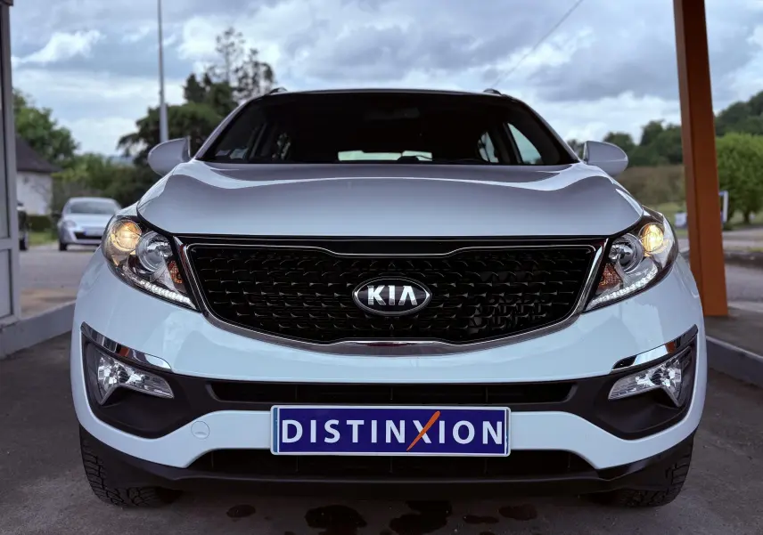 Vue frontale d’un Kia Sportage blanc avec calandre noire et phares allumés sous un abri.