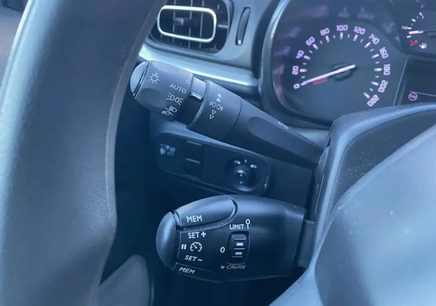 Gros plan sur les commandes au volant d'une Citroën C3 2023 noire, montrant les réglages du régulateur et des phares.