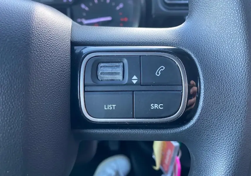 Gros plan sur les commandes audio au volant d’une Citroën C3 2023 noir toit rouge, avec boutons SRC et LIST visibles.