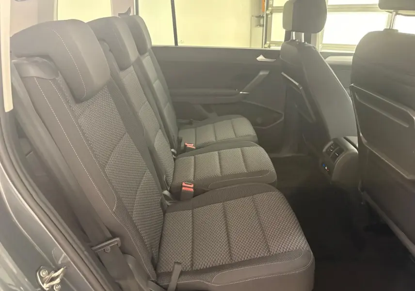 Vue latérale des sièges arrière en tissu gris foncé du Volkswagen Touran 2025 gris dauphin, avec appuie-têtes et ceintures visibles.