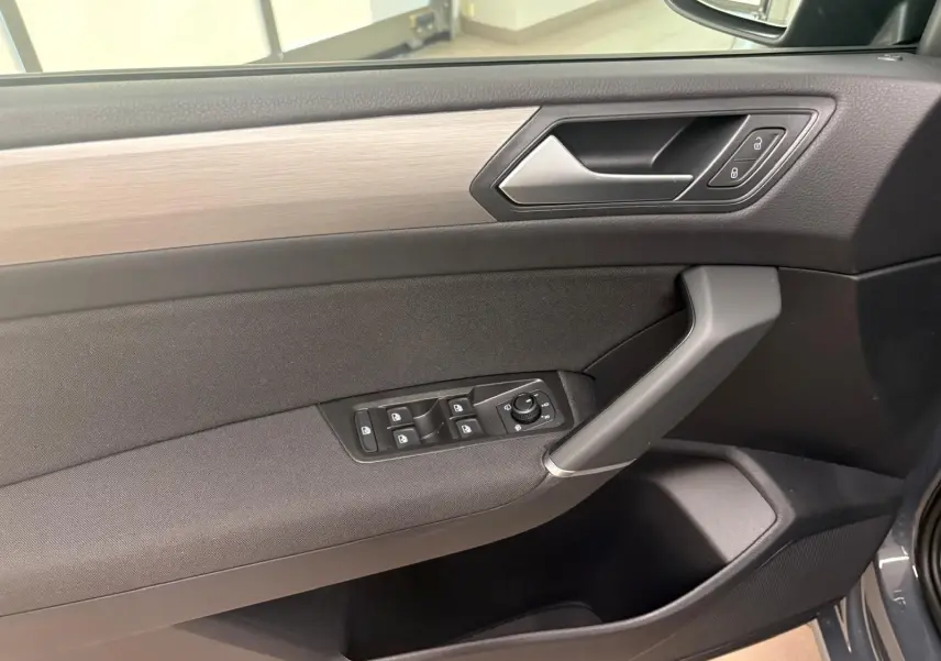 Vue rapprochée de la porte avant gauche du Volkswagen Touran gris Dauphin, avec commandes de vitres et poignée intégrée.