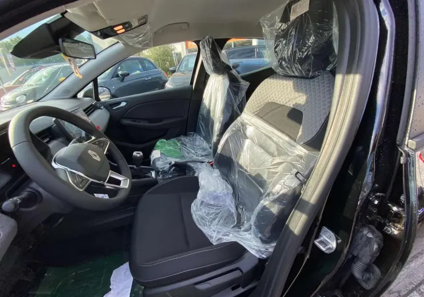 Vue intérieure côté conducteur de la Renault Clio 1.5 Blue dCi noire, sièges protégés par film plastique, volant multifonction visible.