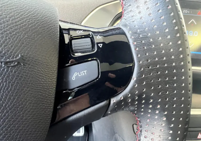 Gros plan sur le volant cuir perforé avec commandes intégrées du Peugeot 308 GT Line rouge de 2019.