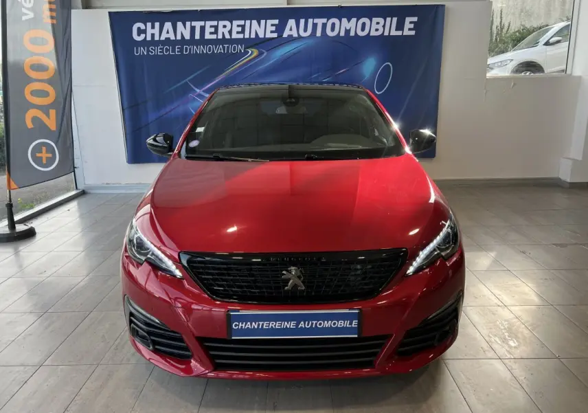 Vue frontale d'une Peugeot 308 Puretech 130 S&S GT Line rouge brillante en showroom avec calandre noire et phares LED.