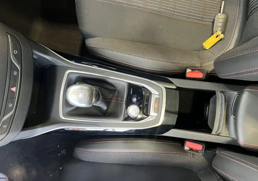 Vue plongeante sur la console centrale et levier de vitesse manuelle d'une Peugeot 308 GT Line rouge, avec clé posée sur siège.