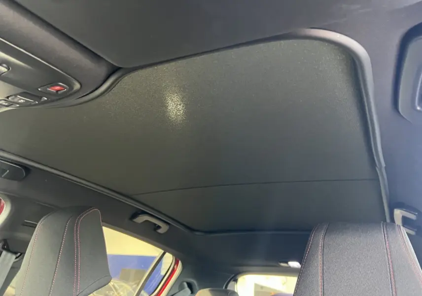 Vue intérieure du toit noir et des appuie-têtes avant avec surpiqûres rouges d'une Peugeot 308 GT Line rouge.