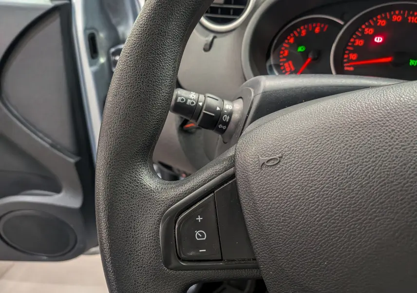 Gros plan sur le volant noir du Renault Kangoo Express 2021 avec commandes intégrées et tableau de bord éclairé en rouge.