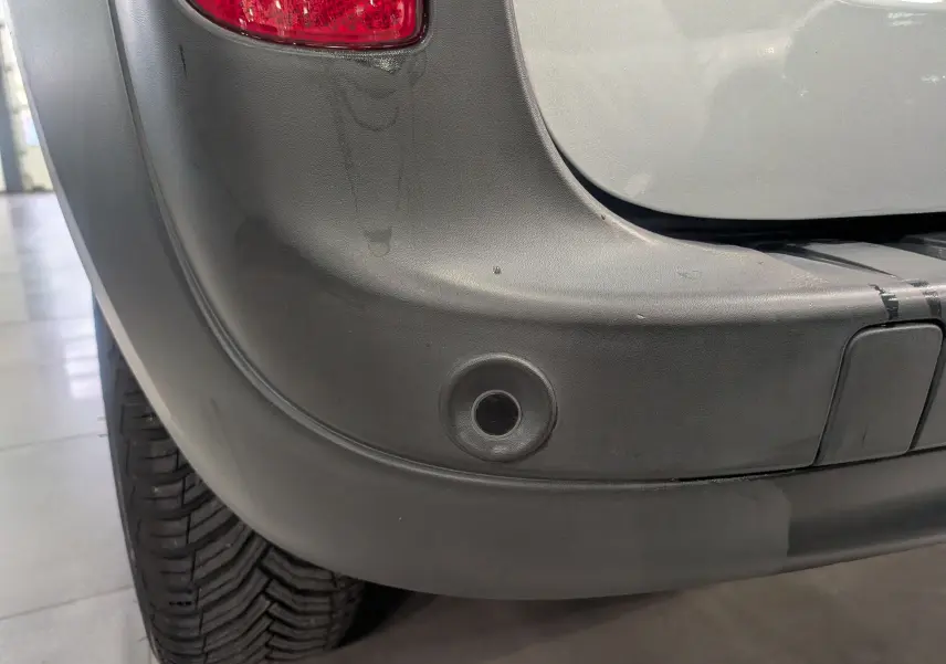 Gros plan sur le pare-chocs arrière gris Highland du Renault Kangoo Express avec feu arrière et capteur de recul visible.