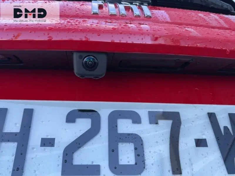 Gros plan sur la caméra de recul et la plaque d'immatriculation d'une FIAT 600 rouge sous la pluie.