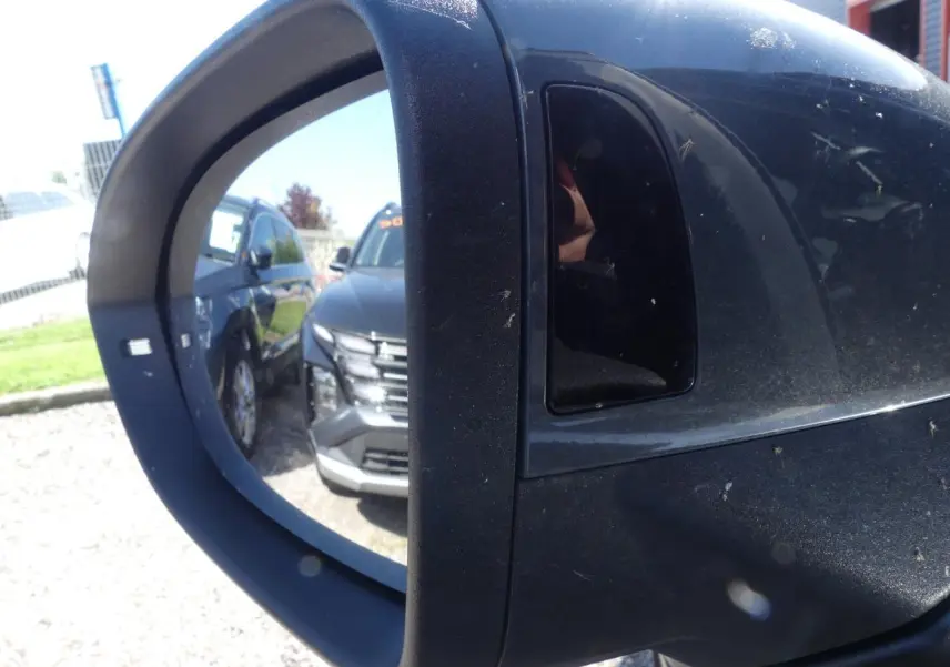 Rétroviseur extérieur droit noir avec reflet d'un SUV gris foncé garé à côté sur un parking.