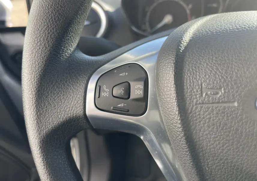 Gros plan sur le volant en cuir noir de la Ford Fiesta 2014 gris titane, avec commandes audio intégrées côté gauche.