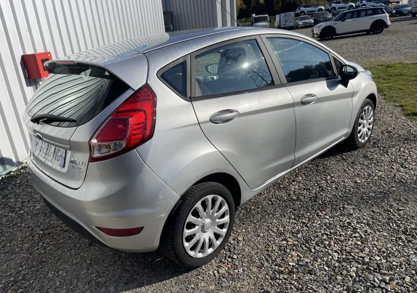 Vue 3/4 arrière droite d'une Ford Fiesta gris titane 2014, compacte avec feux arrière rouges et jantes argentées.