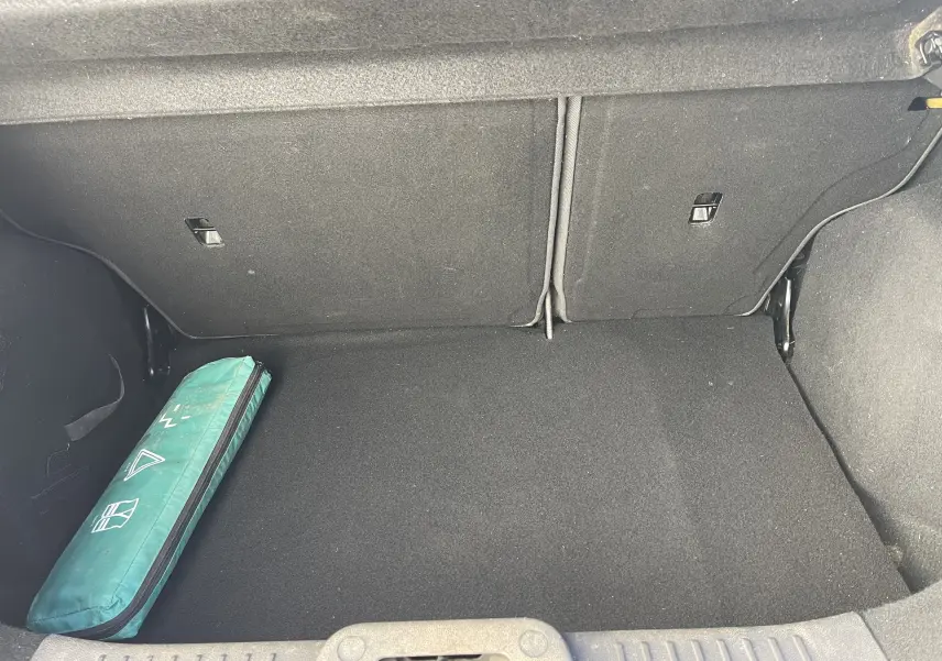 Coffre ouvert d'une Ford Fiesta gris titane 2014, montrant un kit de sécurité vert à gauche sur la moquette noire.
