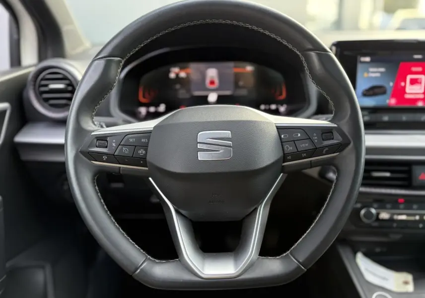 Gros plan sur le volant cuir multifonction à méplat de la SEAT IBIZA TSI 115 Xcellence, tableau de bord numérique visible.