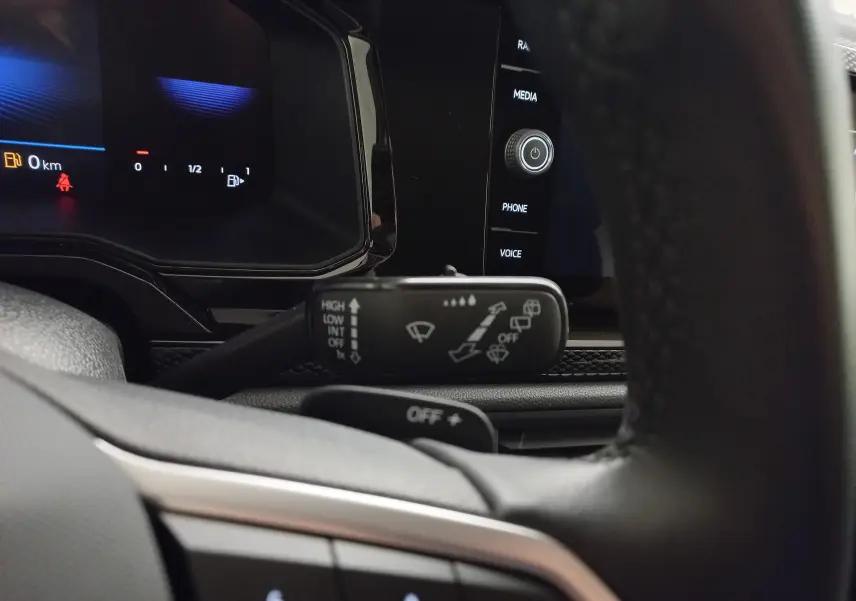 Gros plan sur le commodo d'essuie-glace à gauche du volant du Volkswagen Taigo gris cendré, tableau de bord numérique en arrière-plan.