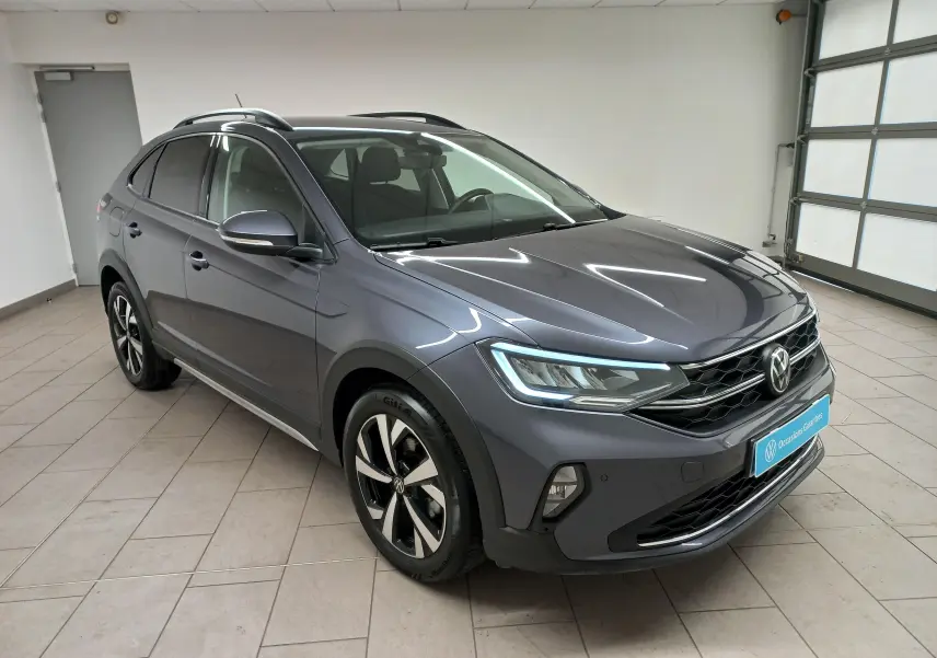 Volkswagen Taigo gris cendré en 3/4 avant droit, avec jantes alliage 17 pouces et projecteurs LED allumés.