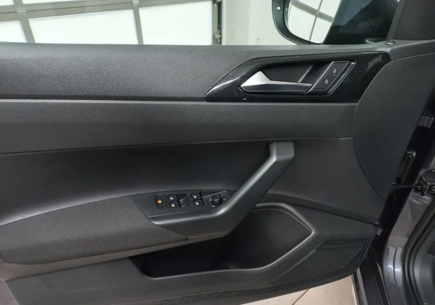 Vue intérieure côté gauche de la porte avant d'une Volkswagen Taigo gris cendré avec commandes électriques et poignée noire.