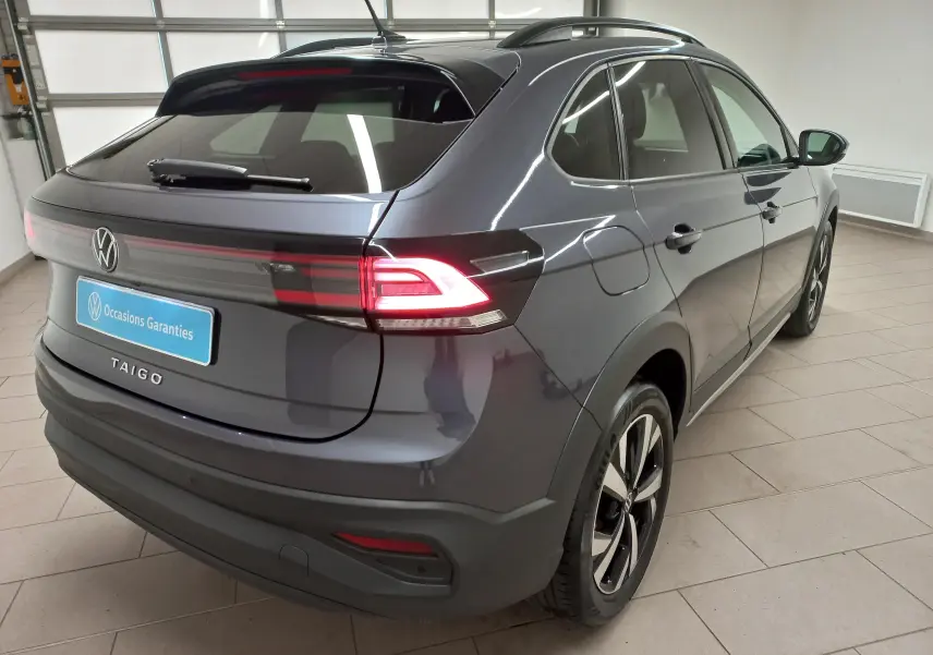 Vue 3/4 arrière droite d'un Volkswagen Taigo gris cendré avec feux arrière LED allumés et jantes alliage Aberdeen 17 pouces.
