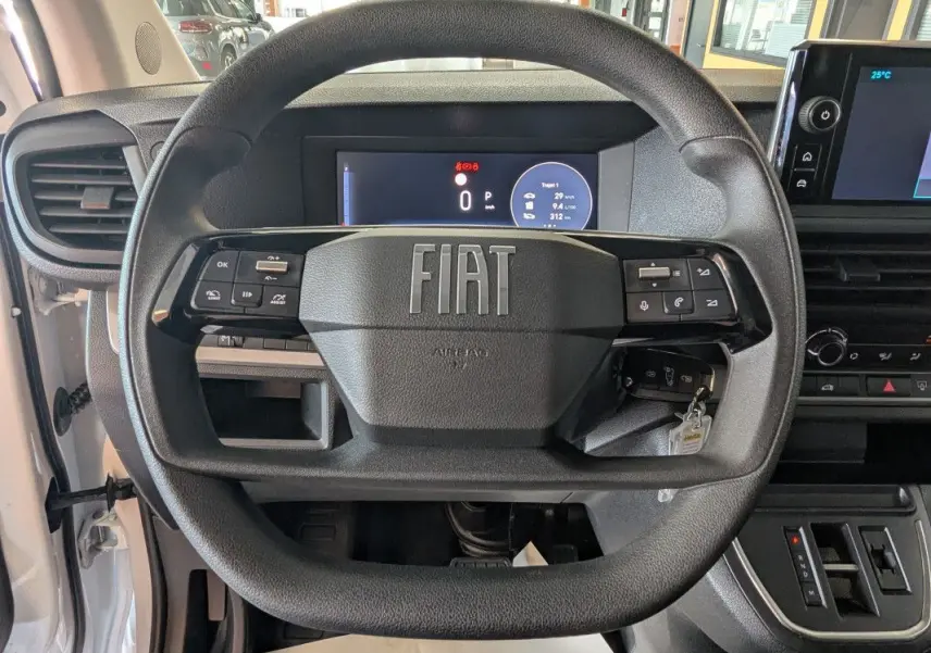 Vue rapprochée du volant noir FIAT du Scudo Fourgon blanc 2025, avec tableau de bord numérique et écran tactile central.